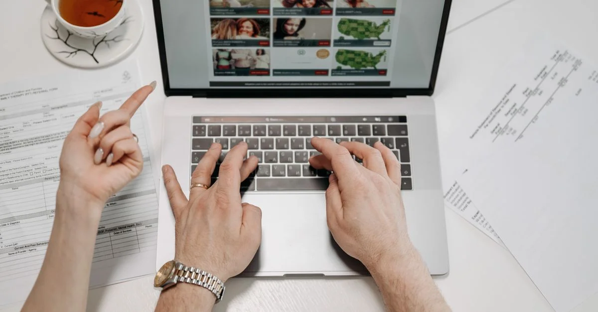 Un gros plan des mains tapant sur un ordinateur portable avec des documents et du thé sur un bureau suggère professionnalisme et concentration.