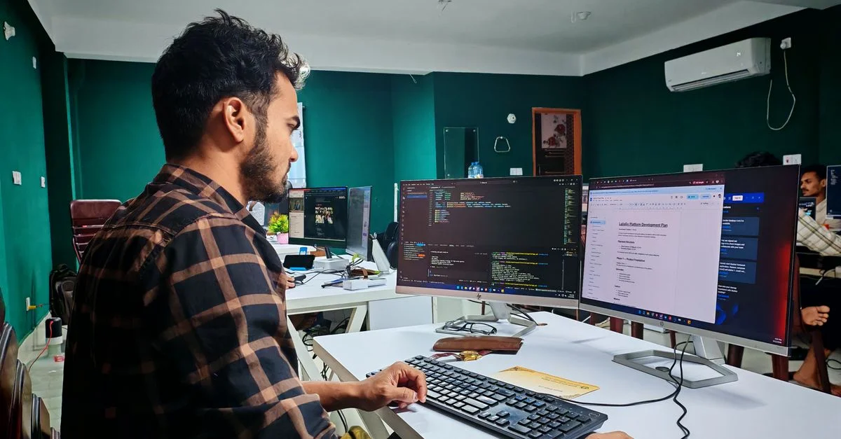 Un développeur de logiciels, concentré et impliqué, code sur deux écrans dans un bureau moderne et bien éclairé.