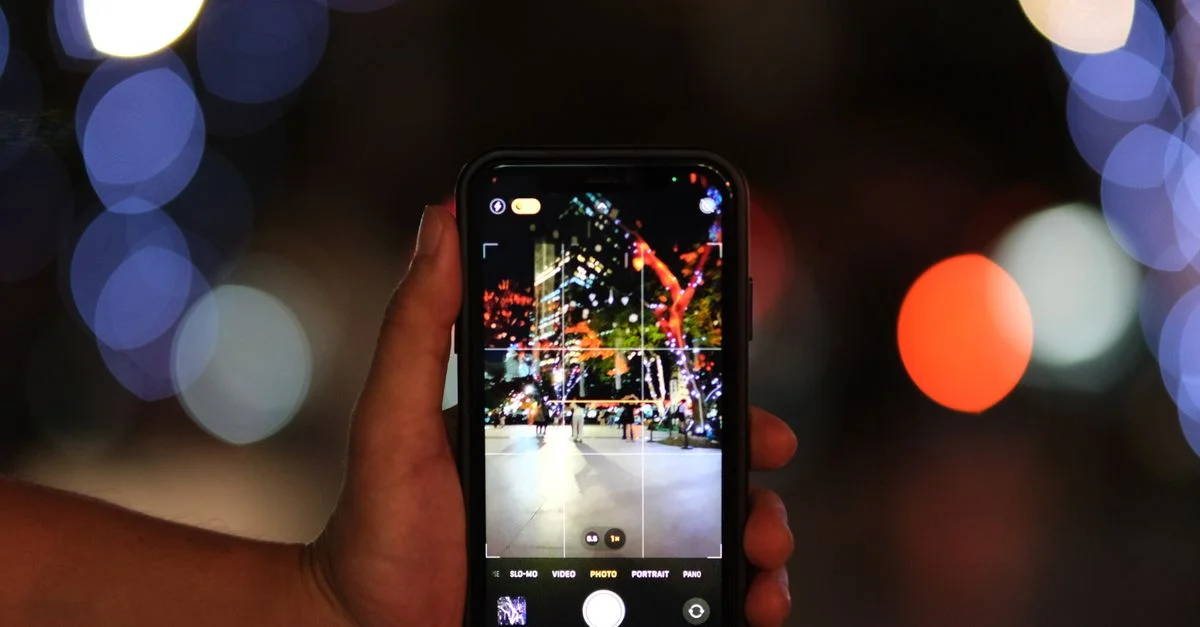 Gros plan sur un smartphone capturant une scène urbaine vibrante avec des lumières bokeh colorées la nuit.