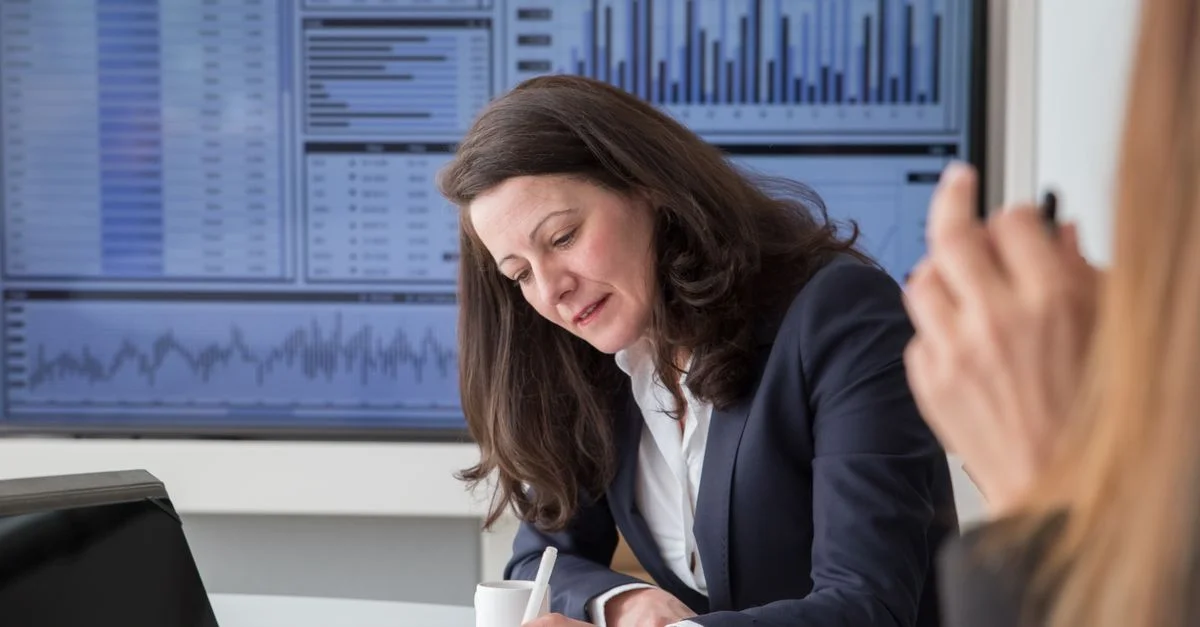 Une femme d'affaires concentrée analysant des données dans un environnement de bureau avec un écran de statistiques.