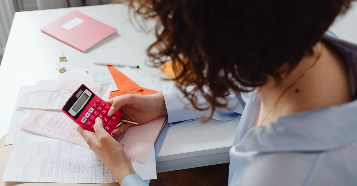 Femme calculant des dépenses avec des documents et une calculatrice sur un bureau.