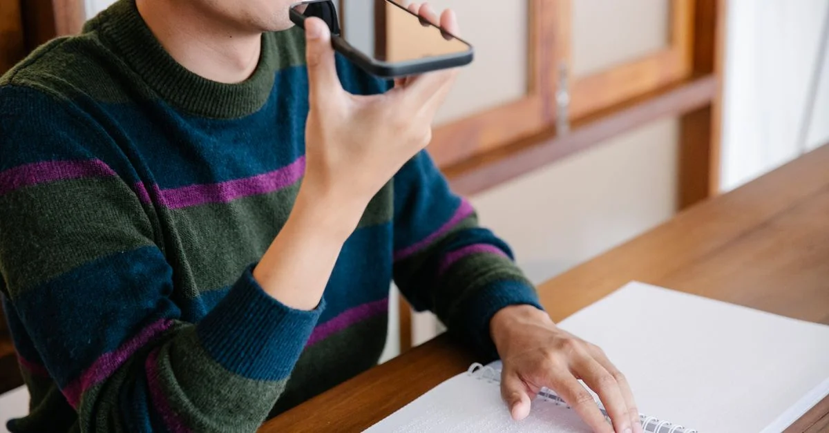 Homme adulte utilisant un smartphone pour des commandes vocales, souriant à son bureau à domicile.