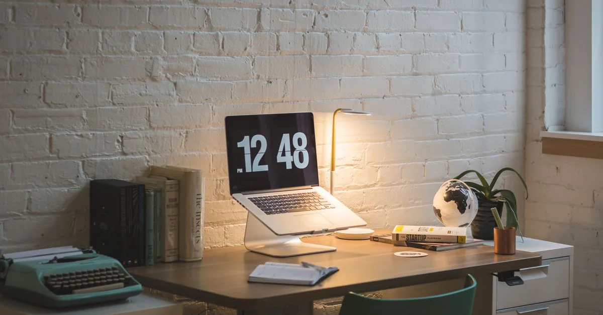 Un espace de travail bien organisé avec un ordinateur portable, des livres et une lampe sur un bureau en bois.