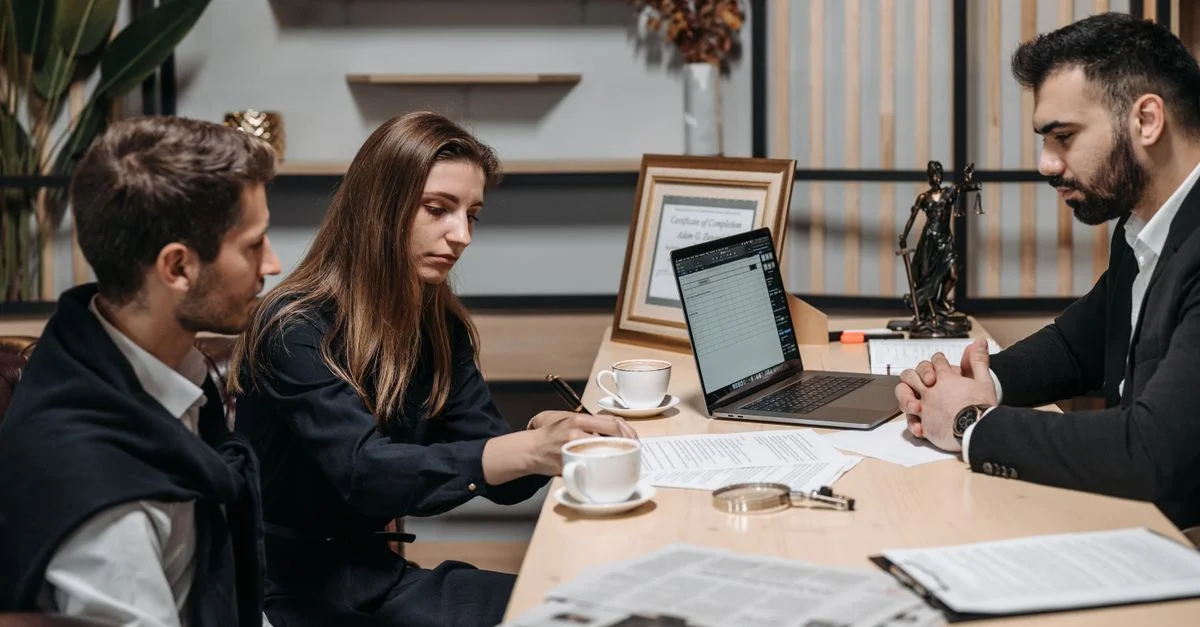 Trois professionnels discutant de documents autour d'un café dans un cadre de bureau moderne.